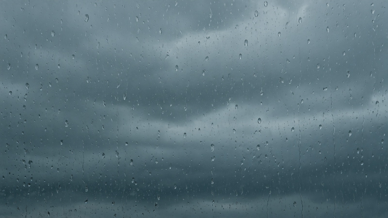 温暖前線の地雨。雨粒のついた窓越しに見る、乱層雲におおわれた空